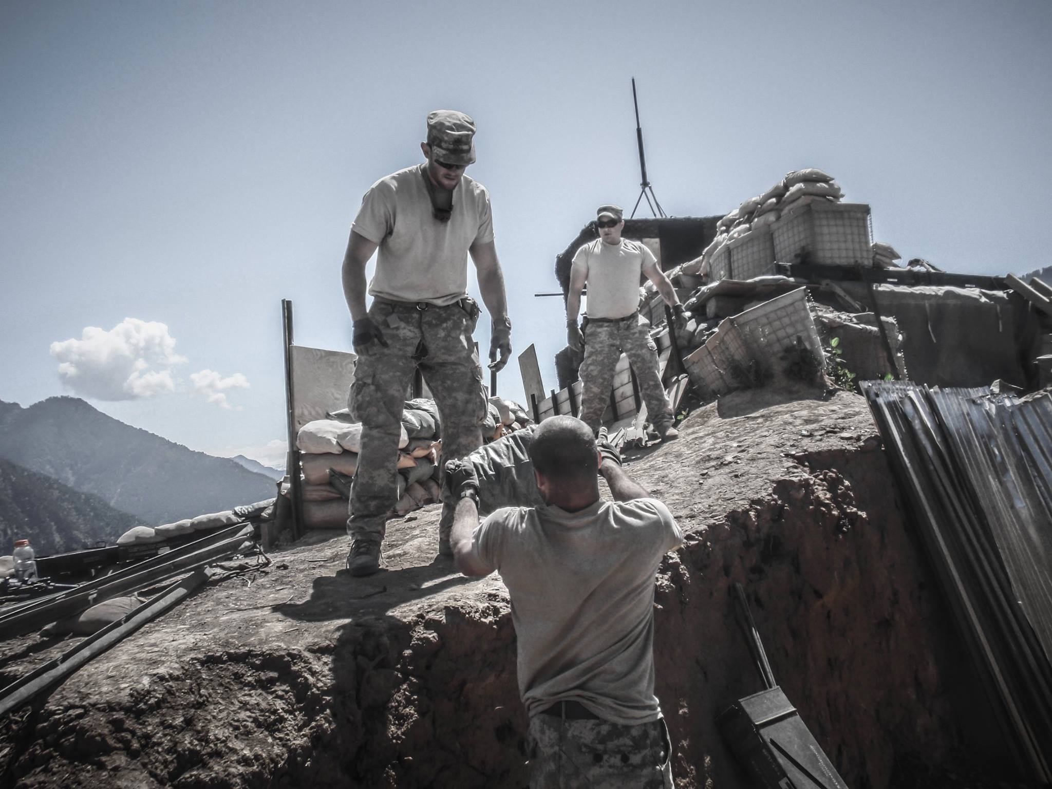 One soldier reaches down to pull another up over a sandbagged wall at a combat outpost.